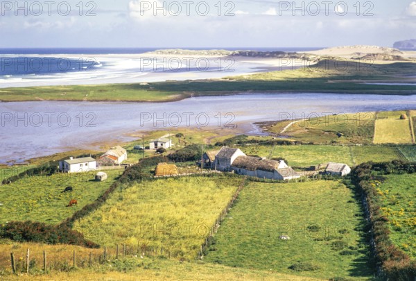 View over thatched farmhouse buildings to Magheraroarty Beach, Meenlaragh, County Donegal, Ireland 1971