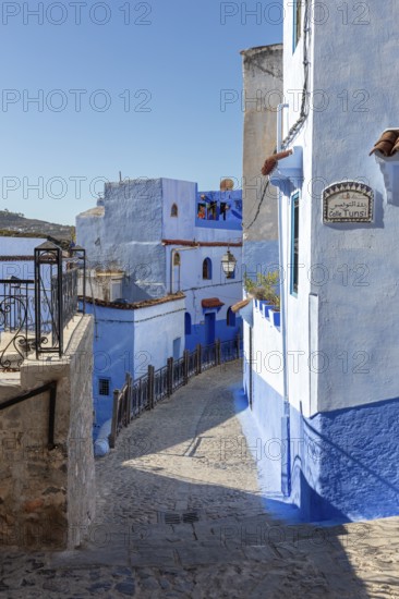 Narrow, winding street in a city with characteristic blue and white buildings under clear skies, Chefchaouen in Morocco