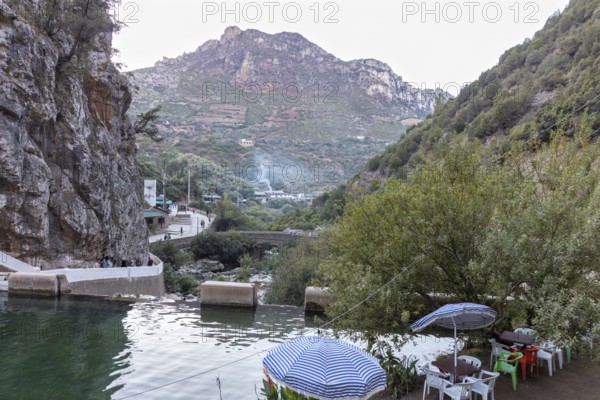 View of a quiet river and road in front of a picturesque mountain panorama with umbrellas, El Kelaa in Morocco