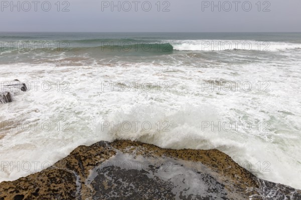 Waves crash over rocks on a grey coast