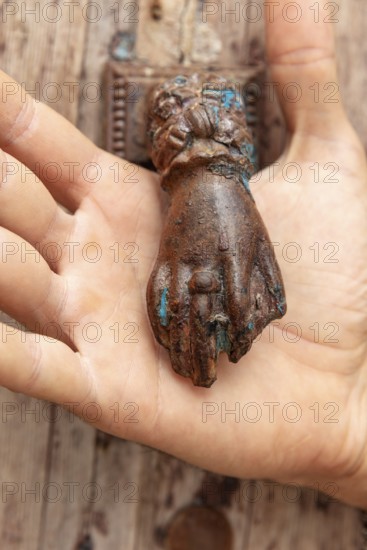 Rusty antique door knocker in the shape of a hand held by one hand
