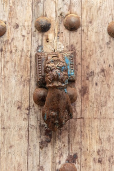 Old door knocker in the shape of a hand on a weathered wooden background