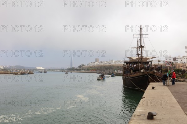 Harbour view with large sailing ship and several boats under cloudy sky