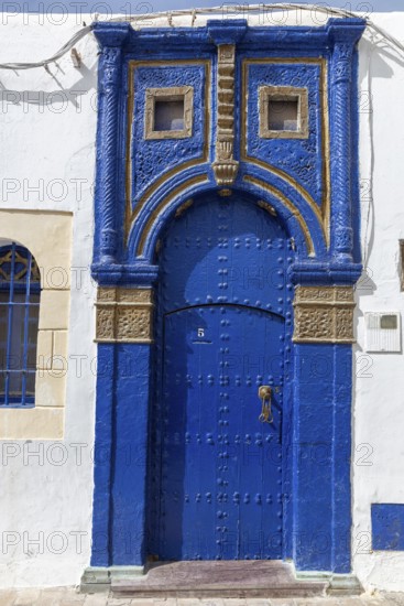 Blue, ornately decorated door in a white wall