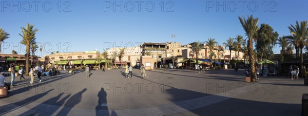 Bustling town square with palm trees and people in sunlight