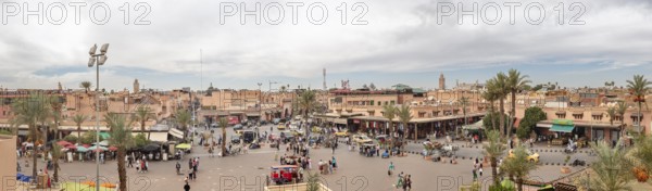 Full marketplace with lots of people and shops, lined with palm trees