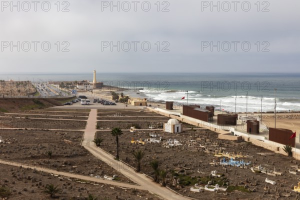 View of coast with cemetery and lighthouse, under cloudy sky