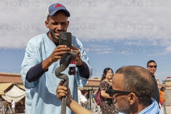 Man photographs a snake on another man's arm in front of an audience