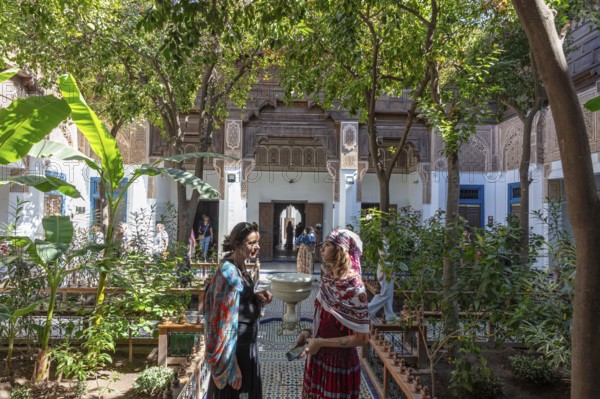 Two woman are talking in the green courtyard of the Bahia Palace with traditional architecture