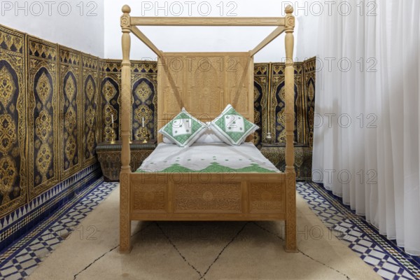 Cozy bedroom with traditional wooden canopy bed and ornate wall decorations, Bahia Palace in Marrakech, Morocco