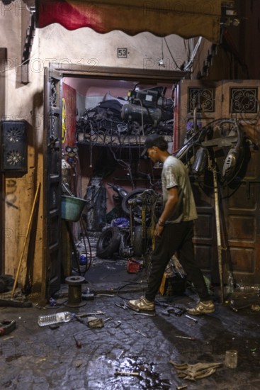 A man works at night in a workshop full of tools and clutter