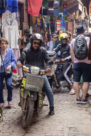 Motorcyclists maneuver through busy, narrow market street full of colors and people