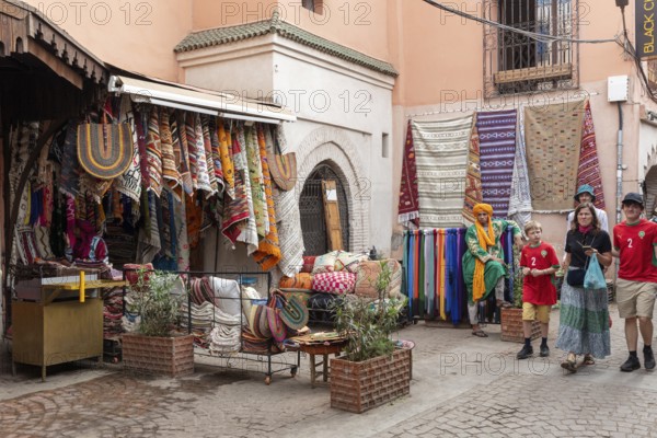 Small street full of colorful textiles in a Moroccan bazaar surrounded by visitors