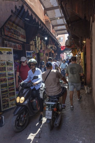 Lively market alleyway with people and scooters in traditional Moroccan style