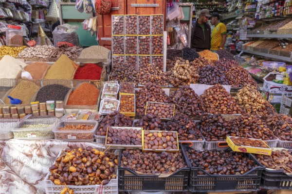Market stand with a variety of spices and dates, surrounded by people