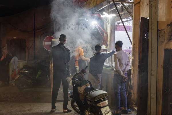 Nocturnal street scene with people, smoke from cooking areas and scooters in a busy area