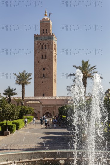 The Koutoubia Mosque in Marrakech, surrounded by palm trees and a sparkling fountain, visited by tourists