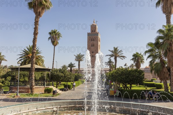 A well-kept garden with a sparkling fountain in front of the majestic Koutoubia Mosque on a sunny day