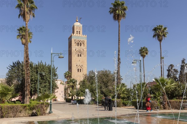 View of the Koutoubia Mosque with bubbling fountains and palm trees against a blue sky