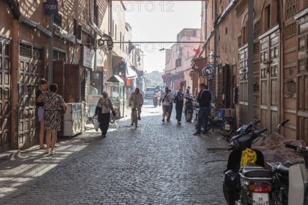 Narrow alley with cobblestones and people under bright sunlight