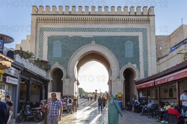 People in front of historic gate with mosaics, cafés along the streets