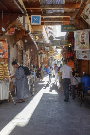 Lively market alleyway with people and traditional stalls in bright light