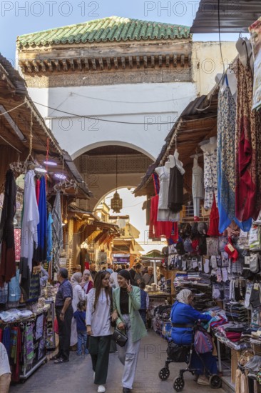 Bustling market corridor with numerous clothes and fabrics under an archway