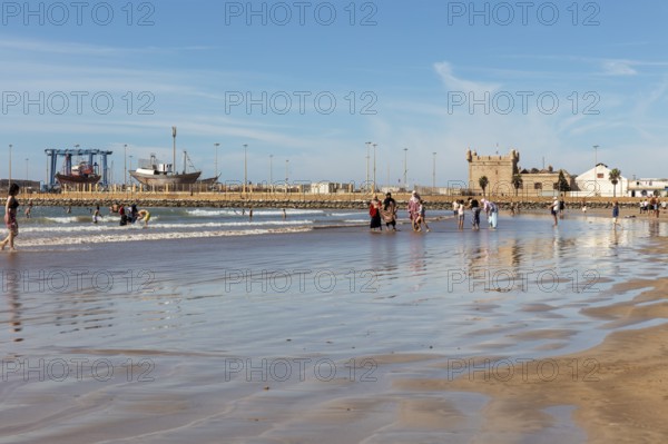 People walking and playing on a city beach under a blue sky