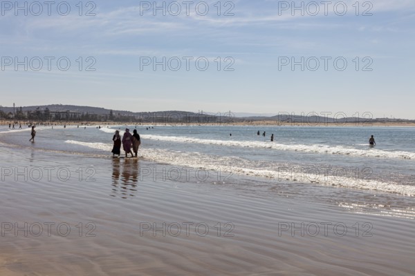 People walking on the beach in shallow water under clear sky