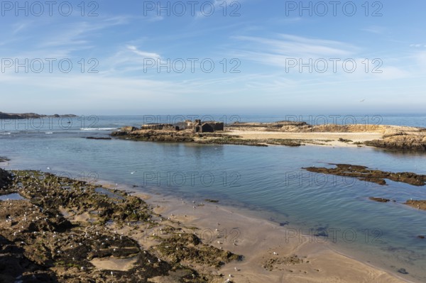 Open coastal landscape with calm sea, rocks and beach under blue sky