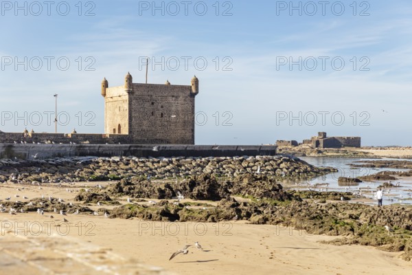 Extensive beach with rocks and historic walls by the sea under clear skies