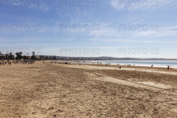 A wide sandy beach with people enjoying the sea and the vast horizon