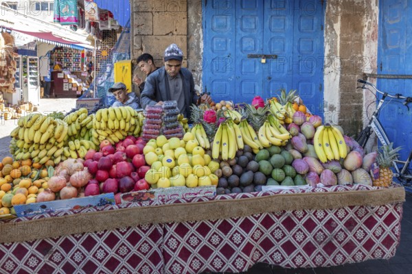 Well-stocked fruit stand with colorful fruits in front of a blue door