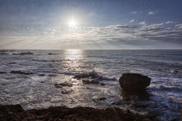 View of the sea at sunset with rocks and waves under a cloudy sky