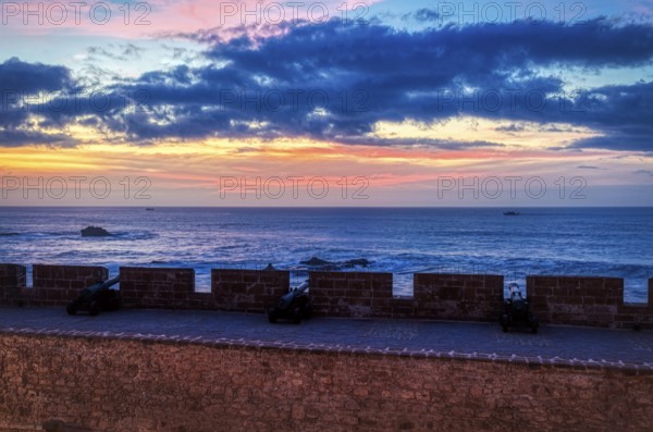 Sunset sky and clouds over the sea behind a historic wall