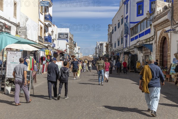Bustling market street with people and numerous shops under a clear blue sky
