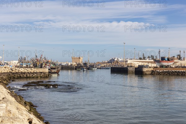 View of a quiet harbor with water, docked boats and a fort in the background