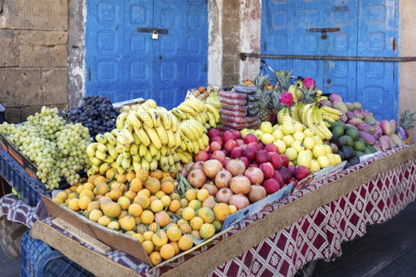 Richly filled fruit stand with colorful fruits in front of a blue door