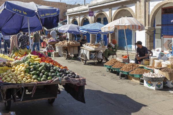 Market scene with colorful fruit and nut stands under protective umbrellas