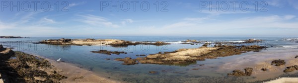 Tranquil coastal scene with shallow water and rocks under clear sky