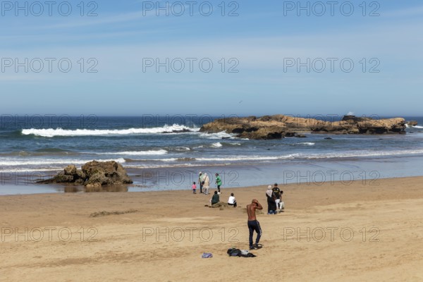 Quiet sandy beach with people and rocks in and around the clear blue sea