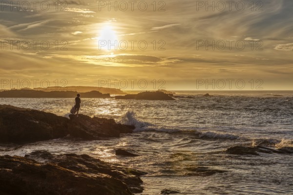 Silhouette of a person on a rock at sunset by the sea