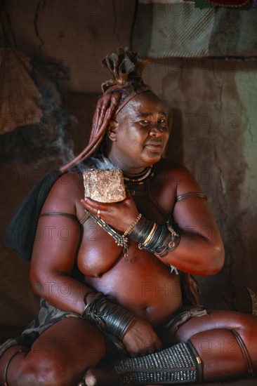 Natural perfume, elderly Himba woman smokes her hair for good smell, in a hut, traditional Himba village, Kaokoveld, Kunene, Namibia