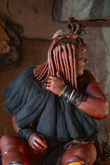 Elderly Himba woman showing her hair and jewelry, in a hut, traditional Himba village, Kaokoveld, Kunene, Namibia