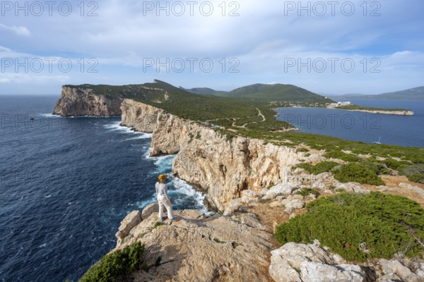 Tourist enjoying the view of steep cliffs by the sea, coastal landscape, cliffs on the Capo Caccia headland, Alghero, Sardinia, Italy