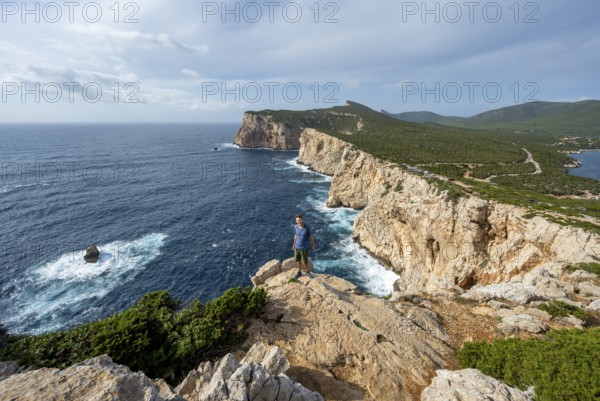 Tourist enjoying the view of steep cliffs by the sea, coastal landscape, cliffs on the Capo Caccia headland, Alghero, Sardinia, Italy