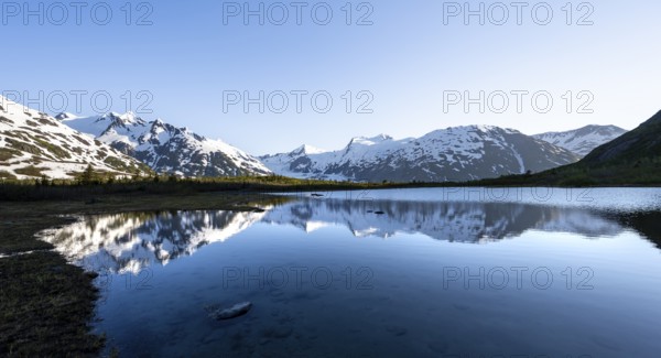 Mountain peaks with Portage Glacier glacier and snow reflected in Divide Lake mountain lake in evening light, Portage Pass Trail, Whittier, Alaska, USA