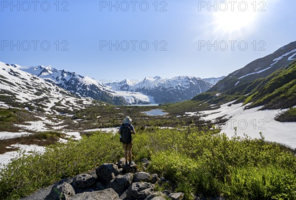 Hiker enjoys views from Portage Pass of Divide Lake, snowy mountain peaks and glaciers Portage Glacier, Portage Pass Trail, near Whittier, Alaska, USA