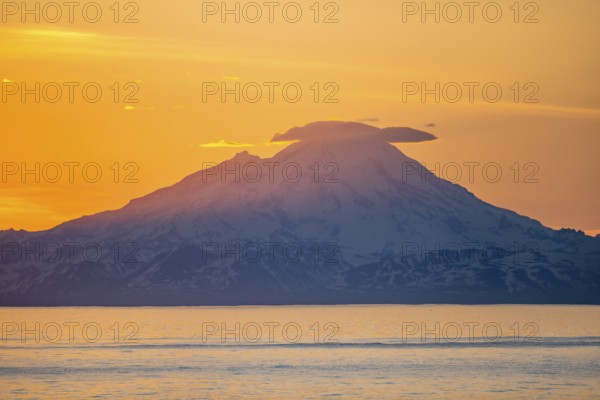 View of Cook Inlet on white mountain peaks of Mount Redoubt at sunset, picturesque golden light of the midnight sun, mountains of the Aleutian Range, Anchor Point, Anchor River State Recreation Area, Alaska, USA