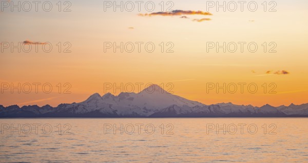 View of Cook Inlet on white mountain peaks of Mount Iliamna at sunset, picturesque golden light of the midnight sun, mountains of the Aleutian Range, Anchor Point, Anchor River State Recreation Area, Alaska, USA